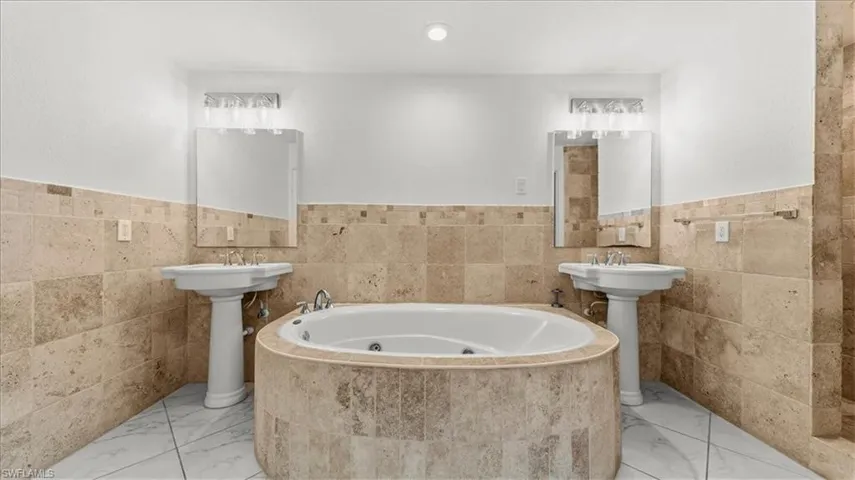 Full bath featuring tile walls, wainscoting, a jetted tub, and marble finish flooring