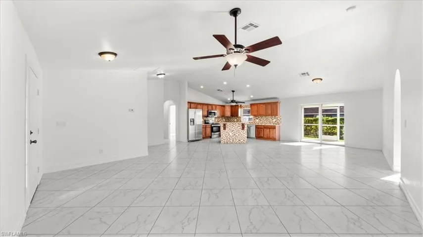 Unfurnished living room with arched walkways, lofted ceiling, ceiling fan, and light marble finish flooring