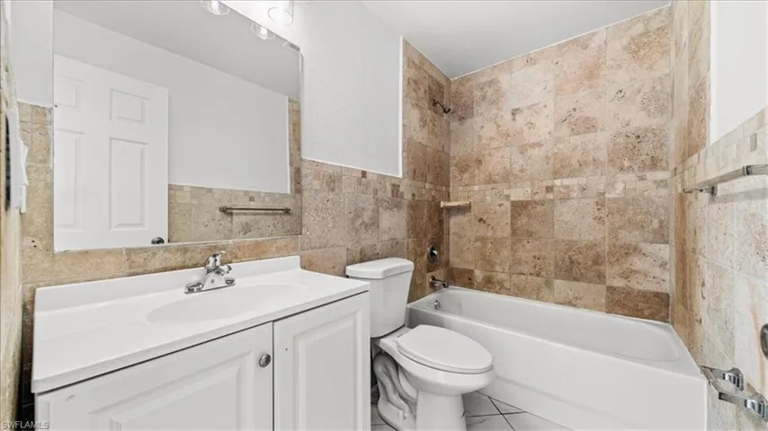 Bathroom featuring tile walls, washtub / shower combination, vanity, and tile patterned floors