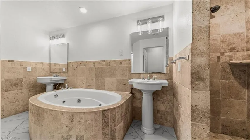 Full bathroom featuring tile walls, a jetted tub, a wainscoted wall, and tiled shower