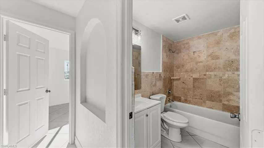 Full bath featuring washtub / shower combination, vanity, and light tile patterned floors