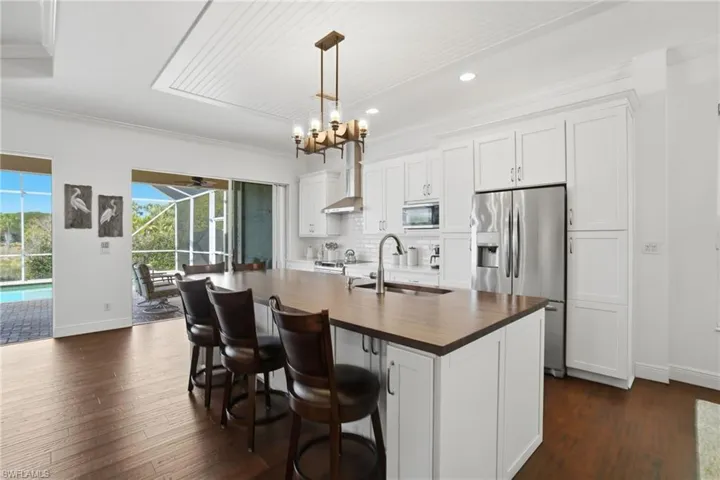 Stunning renovated kitchen with white custom cabinetry & soft close drawers, subway backsplash, butcher board & corian counters, stainless steel appliances, a bead board ceiling accent & adjacent bar with beverage fridge.