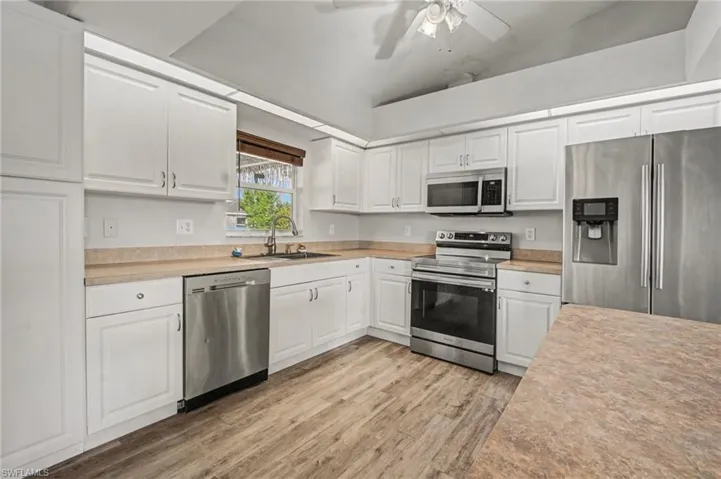 Kitchen with stainless steel appliances, white cabinetry, vaulted ceiling, light countertops, and ceiling fan