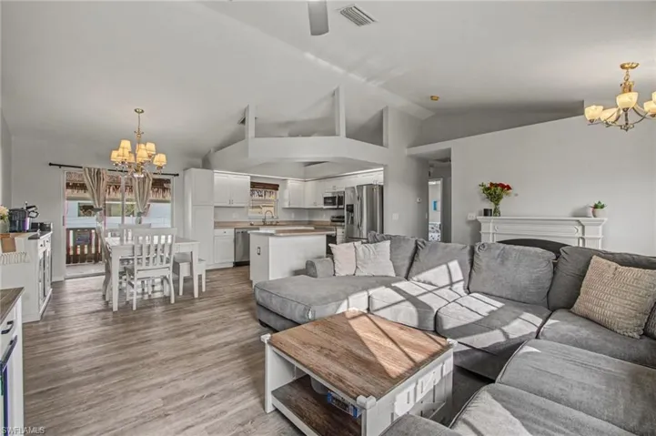 Living room featuring suspended lighting, lofted ceiling, light wood-type flooring, and a ceiling fan