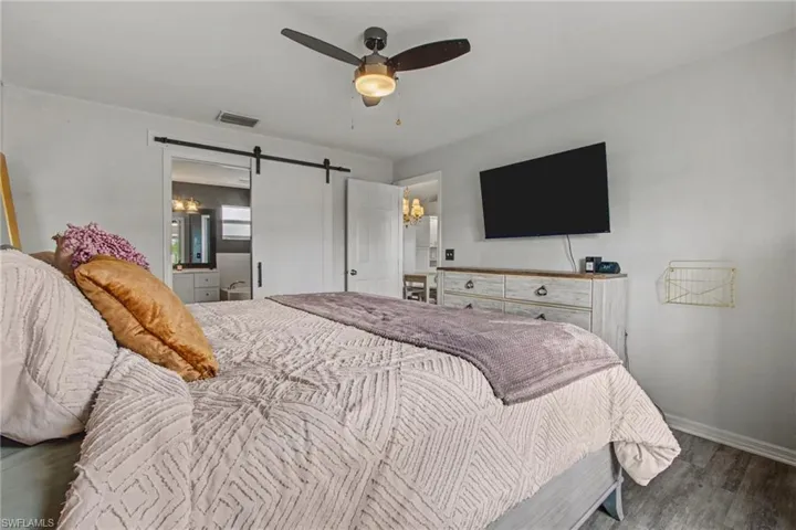 Bedroom featuring a barn door, ensuite bath, wood finished floors, and ceiling fan
