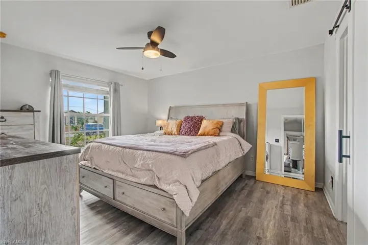 Bedroom featuring dark wood-style floors, a ceiling fan, and a barn door