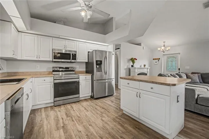 Kitchen featuring open floor plan, stainless steel appliances, white cabinets, ceiling fan, and light wood-type flooring