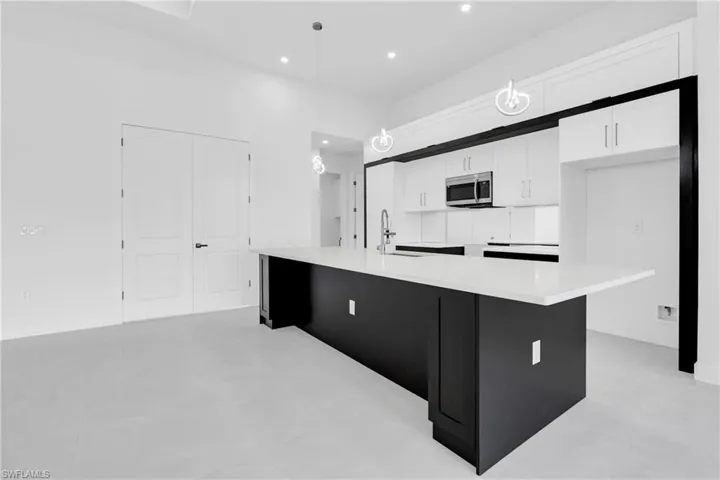 Kitchen with stainless steel microwave, white cabinetry, a large island with sink, recessed lighting, and light countertops