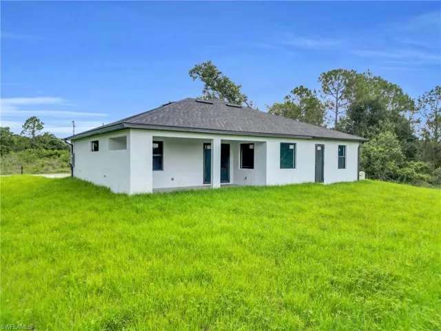 Rear view of property featuring a lawn, stucco siding, and roof with shingles