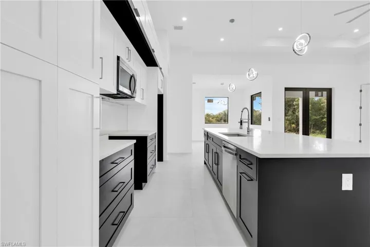 Kitchen featuring appliances with stainless steel finishes, light countertops, white cabinetry, light tile patterned floors, and pendant lighting