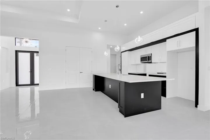 Kitchen with stainless steel microwave, a center island with sink, light countertops, white cabinets, and recessed lighting