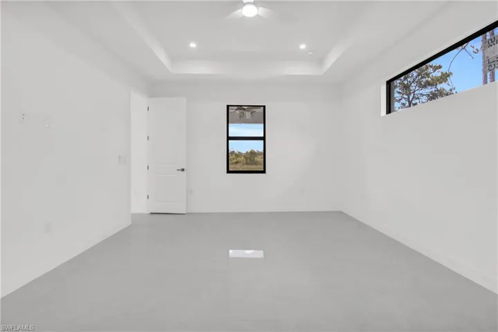 Unfurnished room featuring plenty of natural light, a raised ceiling, a ceiling fan, and recessed lighting