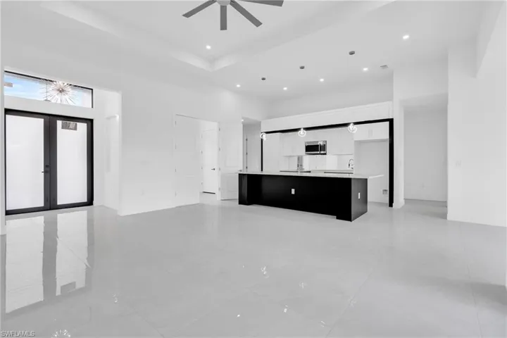 Unfurnished living room with ceiling fan, recessed lighting, a towering ceiling, french doors, and a raised ceiling
