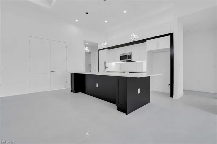 Kitchen with white cabinets, light countertops, a kitchen island with sink, stainless steel microwave, and pendant lighting