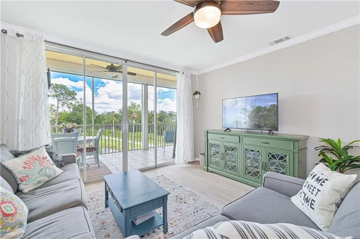 Living room with crown molding, vinyl plank flooring, expansive sliding doors, and ceiling fan