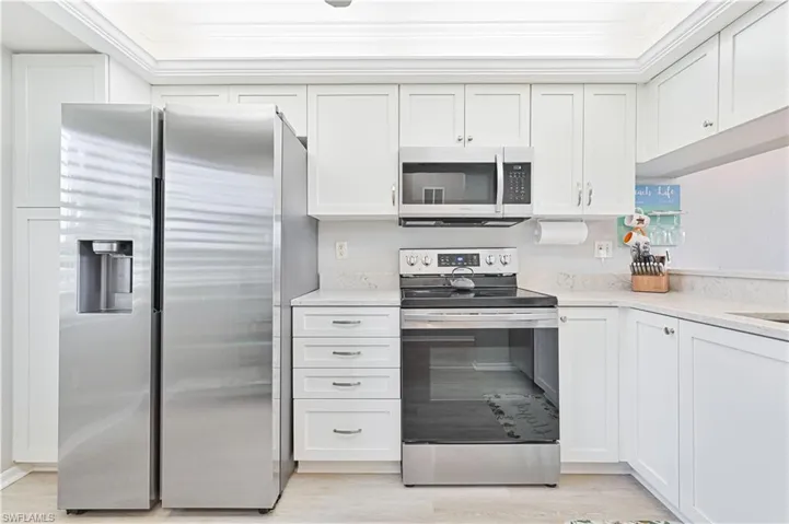 Kitchen featuring stainless steel appliances, white cabinetry, light quartz countertops, light vinyl plank flooring, new tray ceiling.