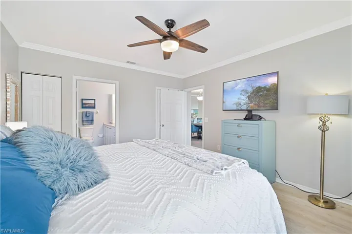 Bedroom featuring ornamental molding, light wood-style flooring, a ceiling fan, ensuite bathroom, and a large walk in closet
