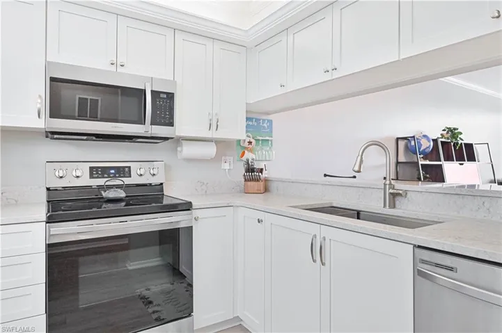 Kitchen featuring stainless steel appliances, white cabinets, quartz countertops, Krauss workstation sink and crown molding