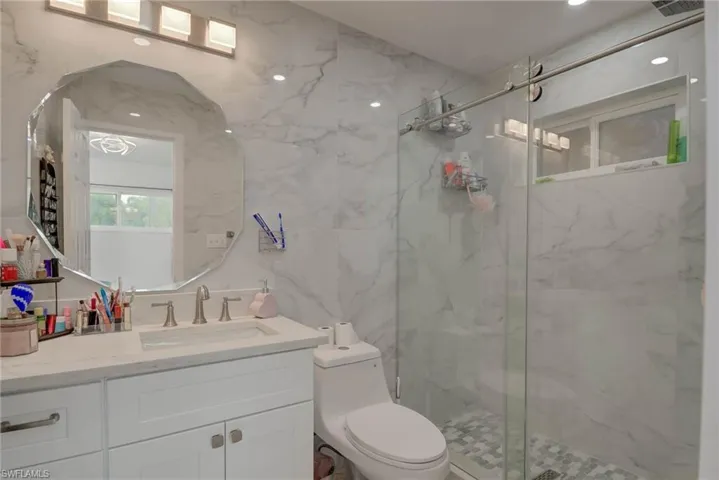 Contemporary bathroom featuring large format marble-look wall tiles, a glass-enclosed shower with a mosaic tile floor, and a white vanity with a rectangular undermount sink
