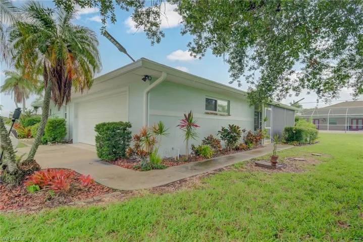 Light-toned stucco exterior featuring a two-car garage, established palm trees, and mature landscaping