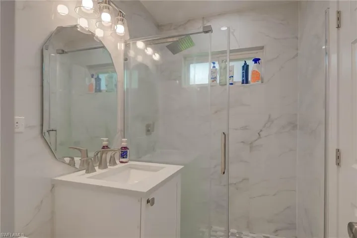 Contemporary bathroom featuring a glass-enclosed shower with marble-look tile, a built-in shower niche, and a window