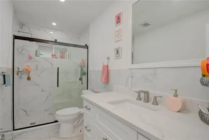 Full bathroom featuring white tile flooring, a shower with a sliding glass door and white marble-look tile surround, a white vanity with a white countertop and integrated sink, and a framed mirror