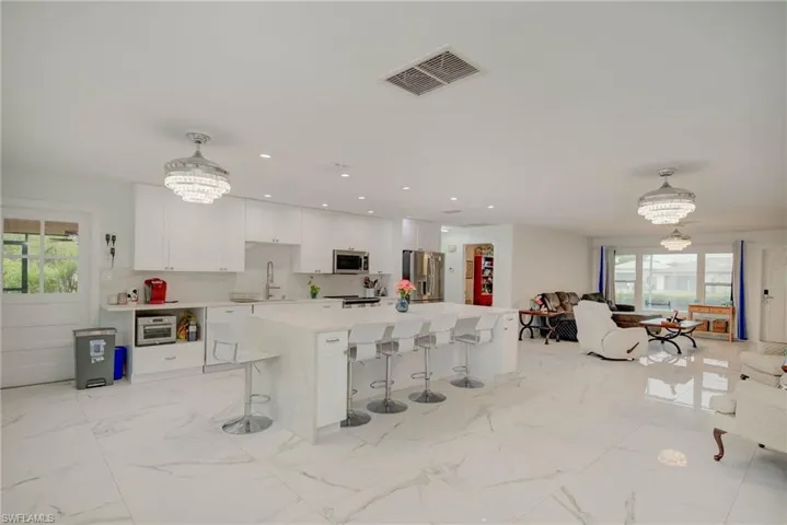 Open-concept interior featuring large format marble-look tile flooring, white shaker cabinetry, an oversized waterfall island with seating, built-in stainless steel appliances, and crystal chandelier-style ceiling fans