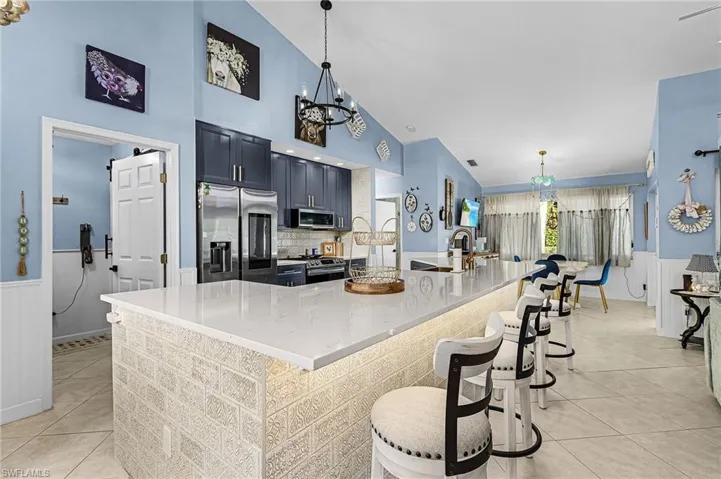 Kitchen featuring wainscoting, stainless steel appliances, a chandelier, hanging light fixtures, and light stone countertops