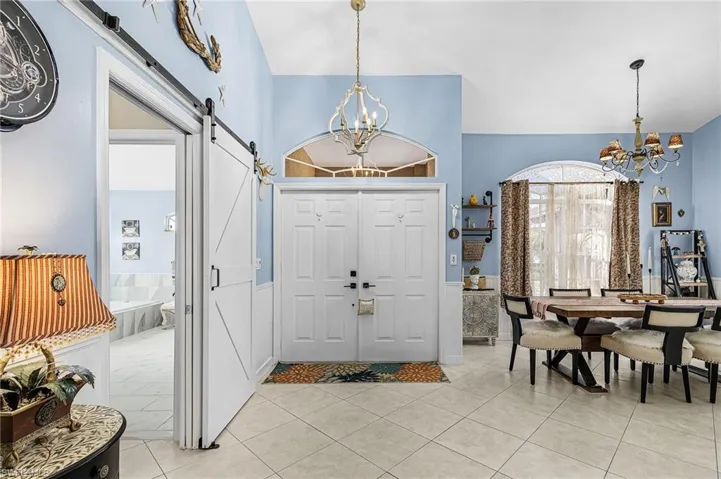 Foyer entrance featuring a chandelier, a barn door, light tile patterned flooring, and lofted ceiling