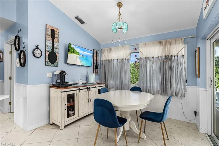 Dining room with a wainscoted wall, vaulted ceiling, and light tile patterned floors