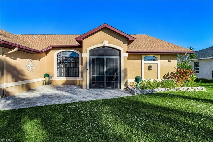 Doorway to property featuring roof with shingles, stucco siding, a yard, and a patio