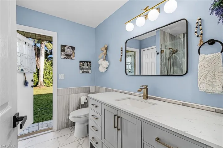 Full bath with vanity, light marble finish flooring, a shower, and a wainscoted wall