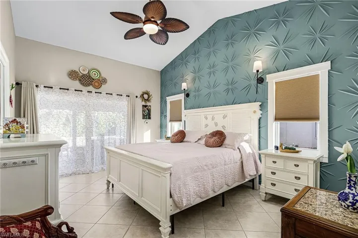 Bedroom featuring vaulted ceiling, light tile patterned floors, ceiling fan, and an accent wall