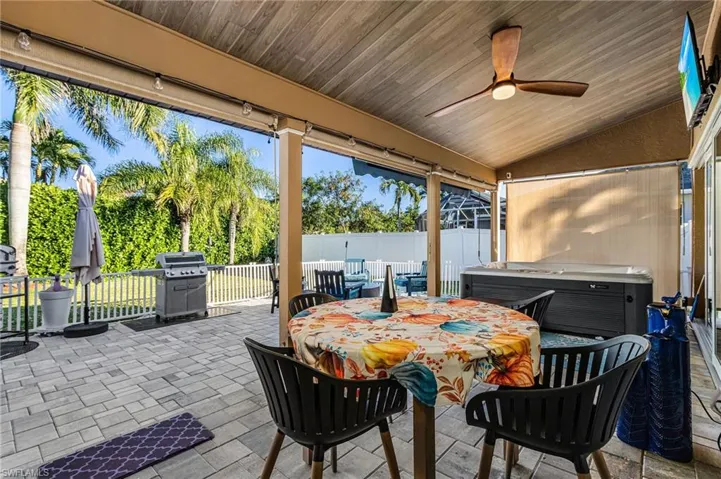 Fenced backyard with a hot tub, outdoor dining area, a patio, ceiling fan, and area for grilling