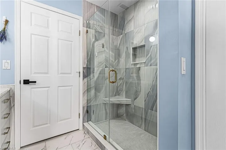 Bathroom with light marble finish flooring, a marble finish shower, and vanity