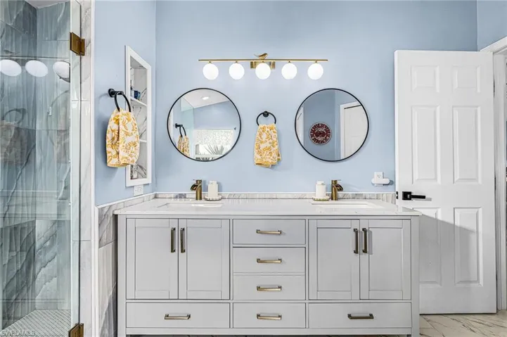 Full bath featuring a marble finish shower and double vanity