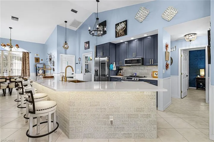 Kitchen featuring a chandelier, appliances with stainless steel finishes, a kitchen bar, decorative light fixtures, and light stone countertops