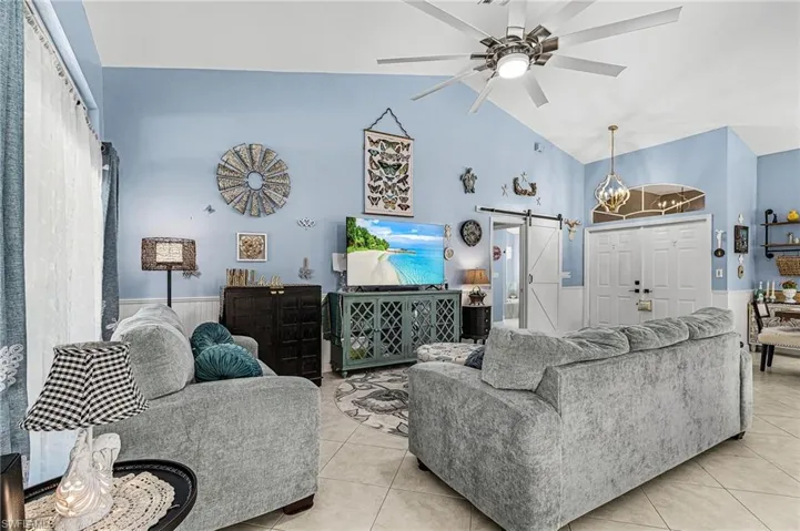 Tiled living room featuring a barn door, wainscoting, a chandelier, a ceiling fan, and high vaulted ceiling