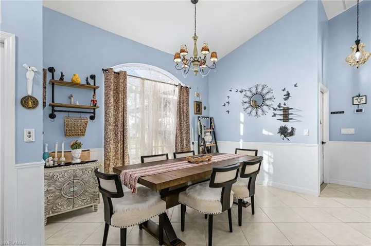 Dining area featuring a chandelier, wainscoting, light tile patterned floors, and high vaulted ceiling