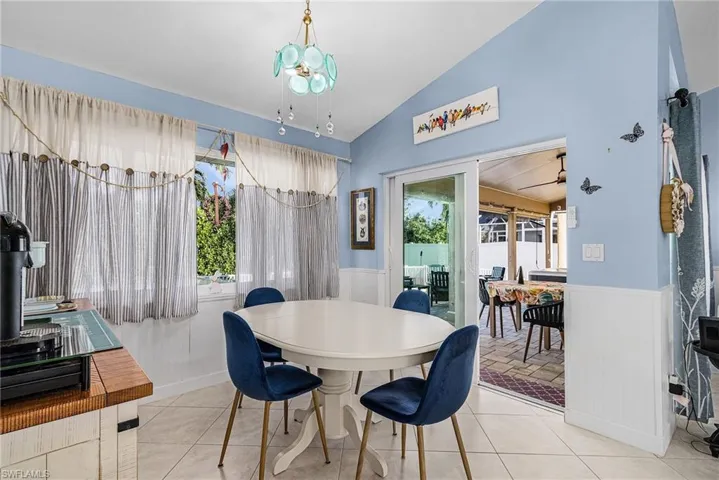 Tiled dining area with lofted ceiling, plenty of natural light, and a wainscoted wall