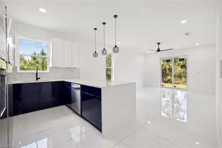 Kitchen featuring decorative light fixtures, kitchen peninsula, decorative backsplash, ceiling fan, and white cabinets
