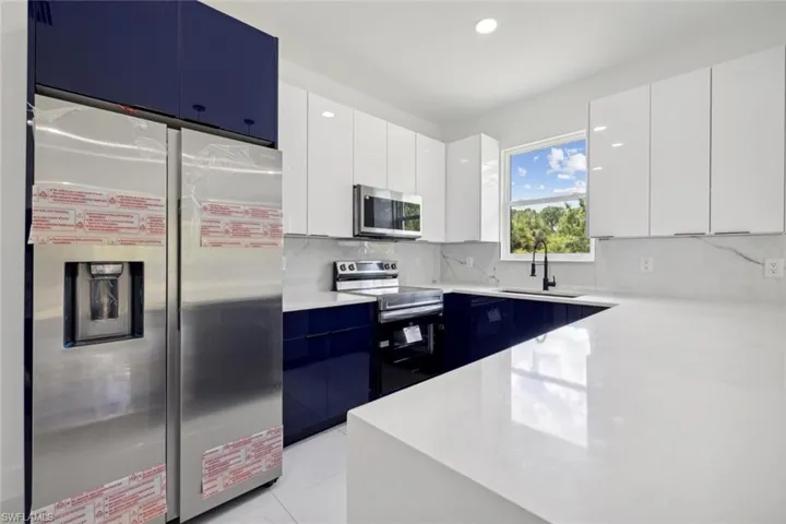 Kitchen with white cabinetry, tasteful backsplash, sink, blue cabinets, and appliances with stainless steel finishes