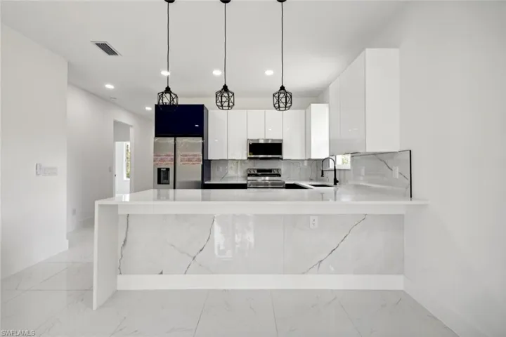 Kitchen featuring decorative light fixtures, tasteful backsplash, stainless steel appliances, sink, and white cabinetry