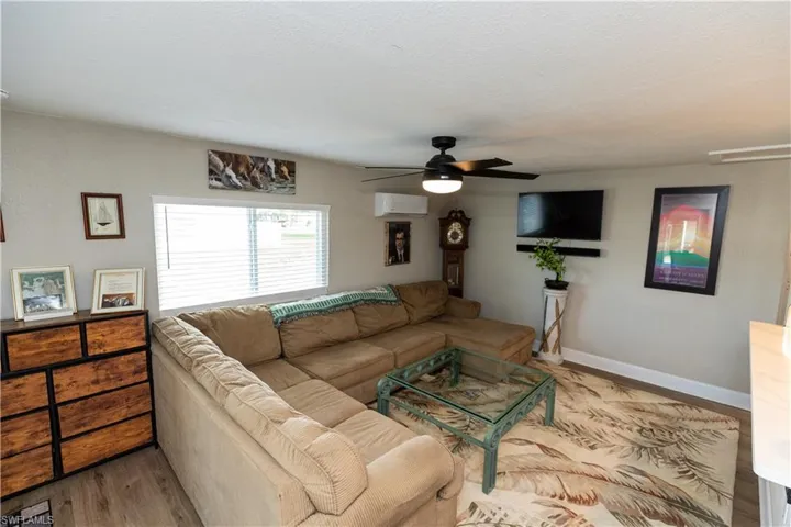 Living area featuring wood-finish flooring, a wall-mounted television, and a ceiling fan with integrated lighting
