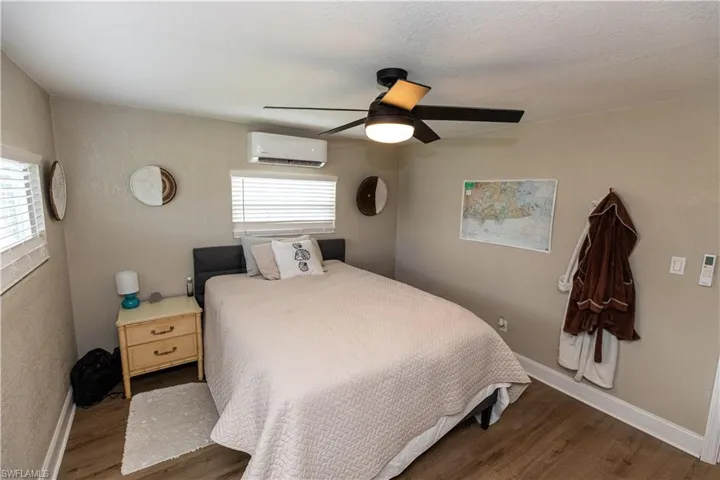 Bedroom featuring wood-finish flooring, a ceiling fan with integrated lighting, and a wall-mounted mini-split AC unit