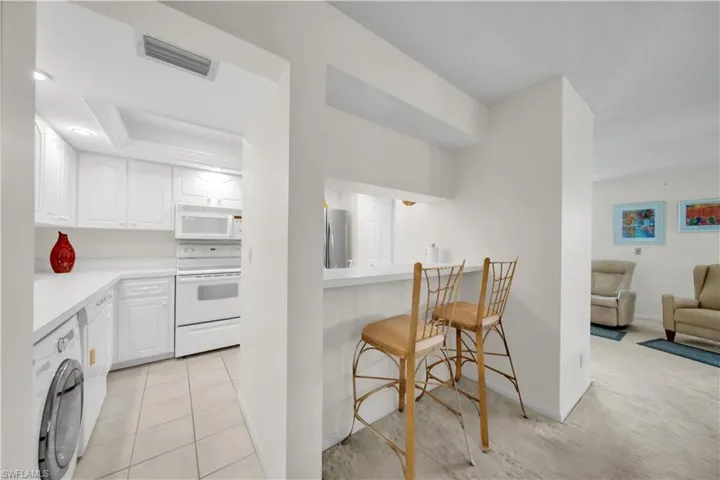 Kitchen featuring a kitchen bar, white cabinetry, light countertops, white appliances, and a tray ceiling