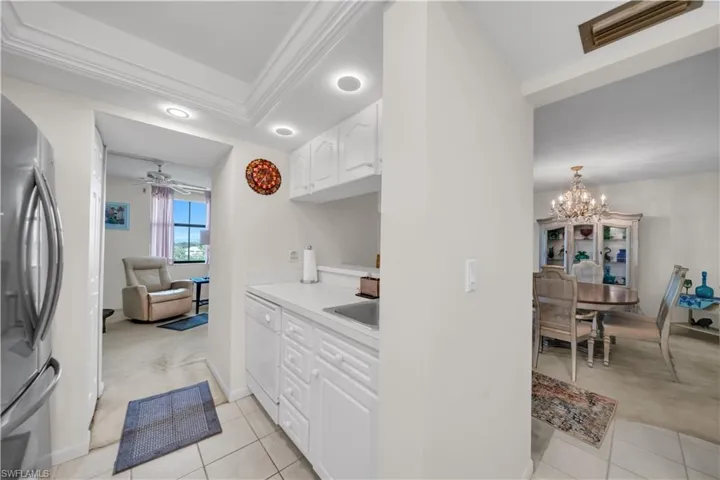 Kitchen with light countertops, freestanding refrigerator, white cabinets, white dishwasher, and crown molding