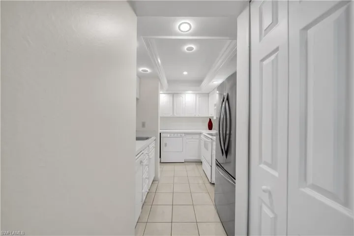Kitchen with light countertops, white cabinetry, freestanding refrigerator, washer / dryer, and white range with electric stovetop