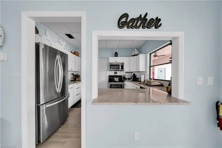 Kitchen featuring light stone counters, stainless steel appliances, white cabinetry, a paneled ceiling, and light wood-type flooring