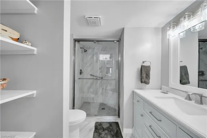 Bathroom with vanity, a marble finish shower, and light marble finish flooring